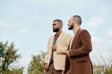 İki erkek model, pitoresk bir alanda güven içinde dikilirken moda sonbahar kıyafetlerini sergiliyor..