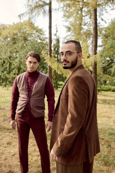 Двое красивых мужчин демонстрируют свой модный осенний наряд в живописном поле, окруженном природой.