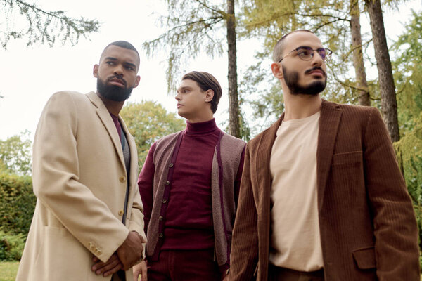 Красота излучает, как трое мужчин демонстрируют свой стильный осенний наряд среди ярких, падающих листьев.