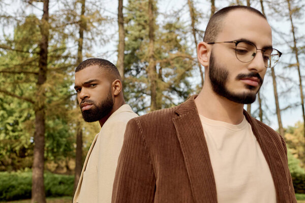 Двое хорошо одетых мужчин задумчиво позируют на живописном осеннем поле, в окружении красочной листвы.