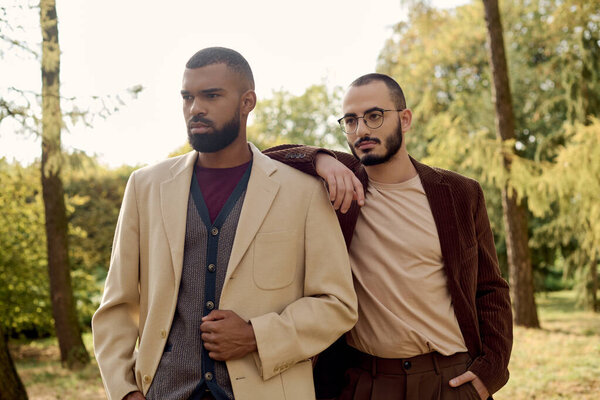 Два модных мужчины стоят вместе в спокойном осеннем поле, источая очарование и стиль в своих нарядах.