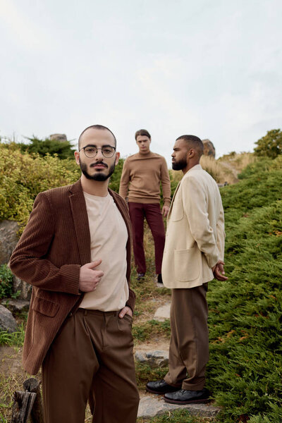 Трое красивых мужчин ставят модные позы на безмятежном осеннем поле, демонстрируя стильные наряды.