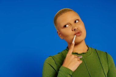 Moda bir görünüşü olan genç bir kadın dudaklarında bir parmak, kendinden emin bir şekilde düşünüyor..