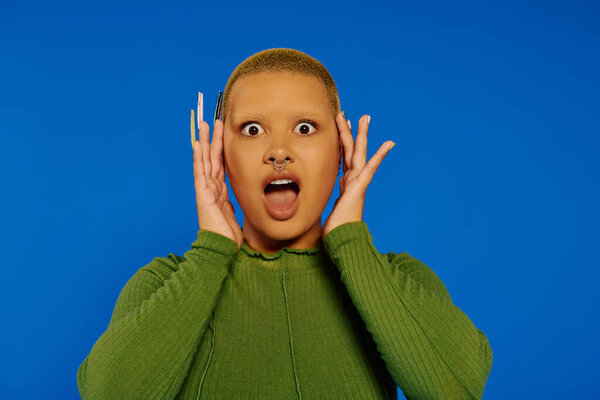 Молодая женщина показывает шокированное выражение лица, обрамляя его руками, излучая энергию.