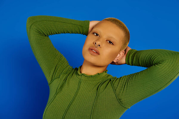 A stylish young woman radiates confidence, flaunting her unique look against a blue backdrop.