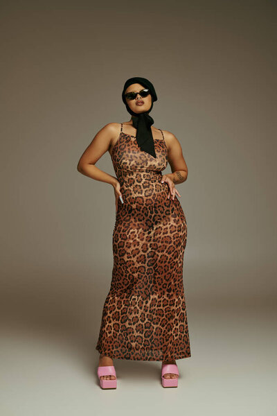Молодая стильная женщина уверенно позирует в леопардовом платье, подчеркивая свое чувство стиля.