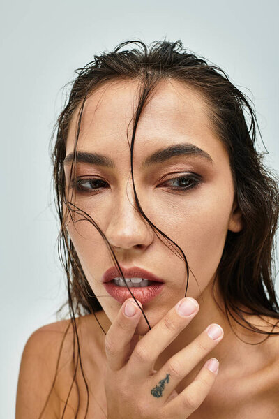 A stunning close up of a woman with long wet hair thoughtfully brushing her face.