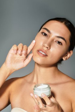 Kadın nazikçe yüzüne krem sürüyor. Güzelliğini ve cildini gösteriyor..