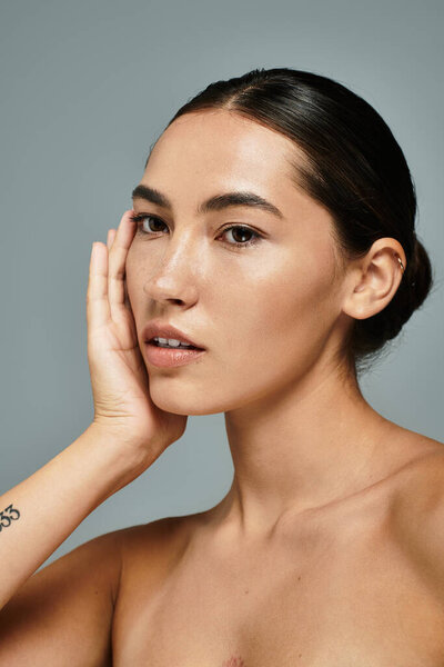 Женщина нежно касается своего лица, излучая уверенность и элегантность на мягком фоне..