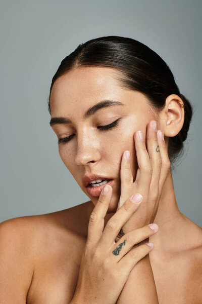 Изящная женщина нежно прикасается к лицу, демонстрируя свои уникальные татуировки и спокойное выражение лица..