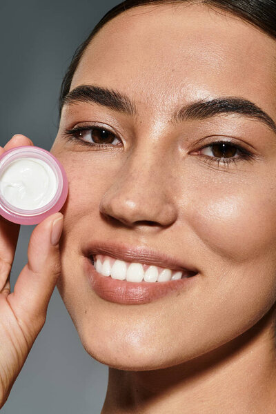 Женщина ярко улыбается, демонстрируя продукт по уходу за кожей, отмечая ритуалы красоты.