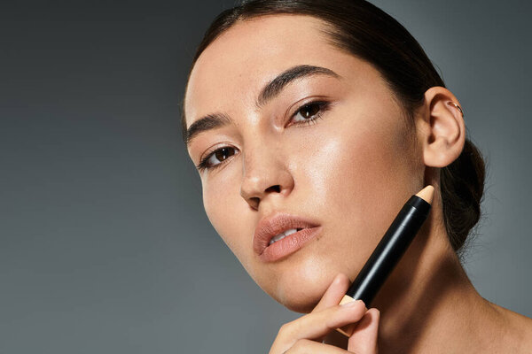 Красивая женщина улучшает свои черты с помощью инструмента макияжа, позируя уверенно.