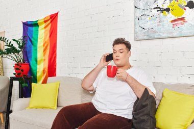 Kanepede dinlenirken, bir kişi kırmızı bardağı tutar ve telefonda neşeli bir şekilde konuşur..