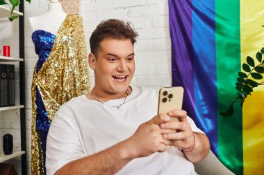 Neşeli bir insan renkli dekorasyon ve kumaşlarla çevrili akıllı bir telefonla etkileşime girer..