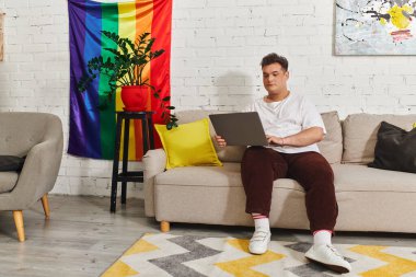 A queer person sits comfortably on a sofa, working on a laptop, surrounded by colorful decor. clipart