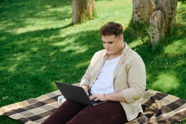 A queer person sits on a blanket, focused on their laptop in a lush green park. clipart