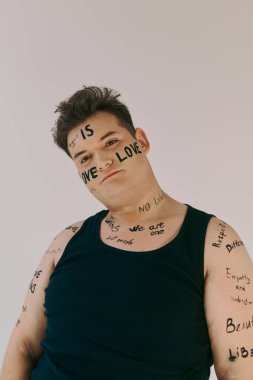 A queer individual showcases body art with empowering messages in a studio space. clipart