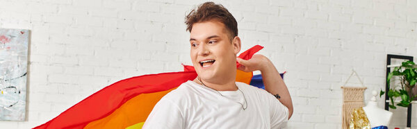 Странный человек с радостью воплощает в себе самовыражение, игриво держа в помещении радужный флаг..