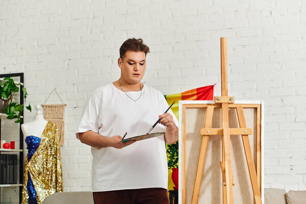 A talented queer individual expresses their artistry while painting on a canvas in a lively studio.
