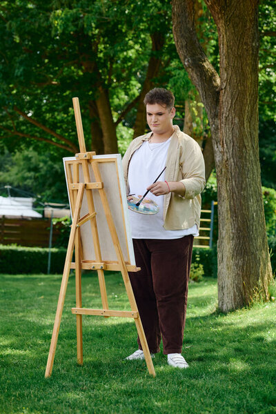 Творческий человек страстно рисует на мольберте в окружении яркой зелени.