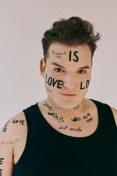A queer person showcases expressive body art featuring messages of love and respect on their skin.