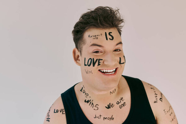 A joyful queer individual showcases expressive body art with uplifting messages written all over.