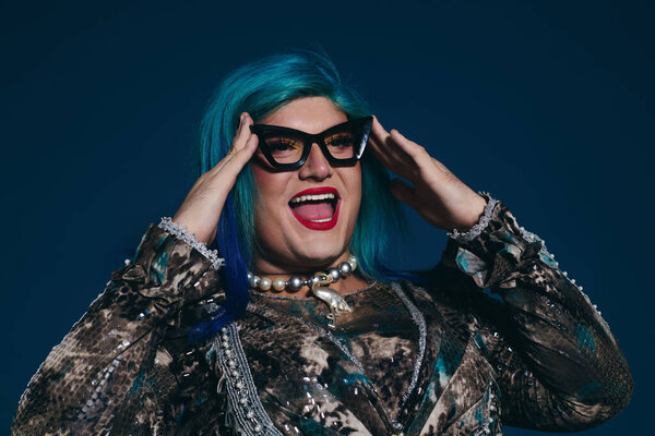 A queer person shines with colorful hair, stylish glasses, and a bold outfit.