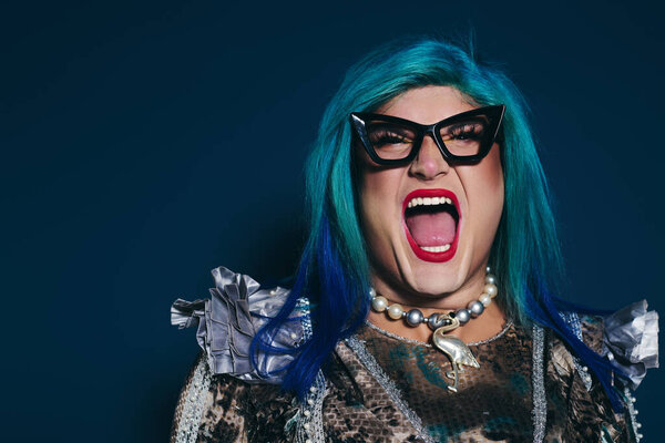 A vibrant queer person with colorful hair joyfully celebrates against a dark backdrop.