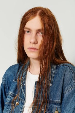 Genç bir çocuk uzun kızıl saçlarını ve kot kıyafetlerini sergileyerek stüdyoda eşsiz tarzını sergiliyor..