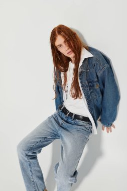 Canlı, uzun kızıl saçlı genç bir çocuk stüdyo ortamında şık bir kot giysisi giyiyor..