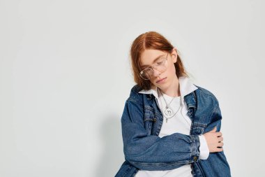 Canlı kızıl saçlı genç bir adam şık bir kotun içinde düşünceli bir şekilde poz veriyor..