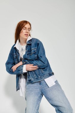 Genç bir çocuk, modern bir stüdyo arkaplanının içinde şık bir kot elbiseyle rahatça poz veriyor..