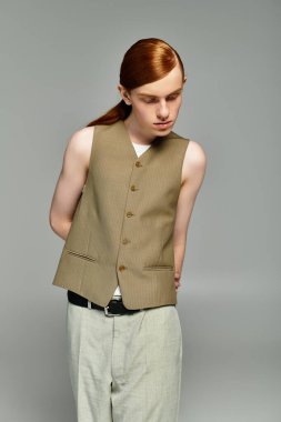 Şık kızıl saçlı genç bir çocuk zarif bir şekilde gri bir arkaplana karşı şık ve şık bir şekilde poz veriyor..