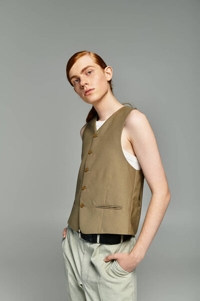 A teen with striking red hair poses fashionably in a chic smart casual outfit against a sleek grey background.