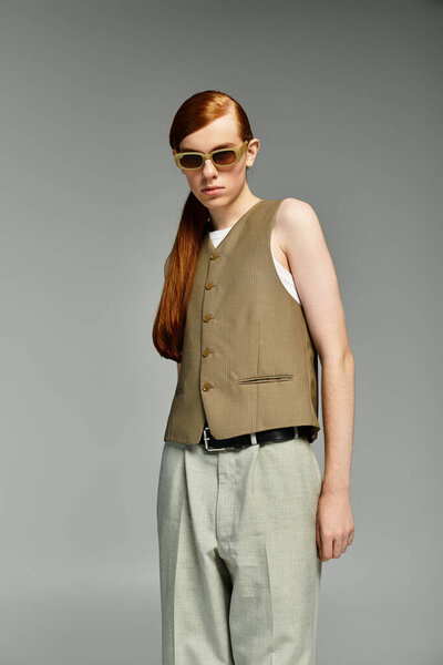 Мальчик-подросток с яркими рыжими волосами уверенно моделирует элегантный повседневный наряд в элегантной серой обстановке.