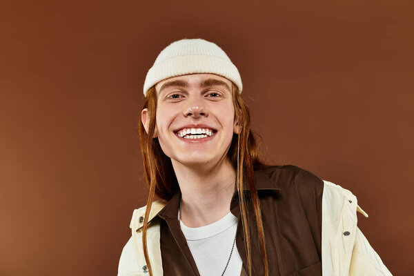 A teenage boy with vibrant red hair showcases a trendy outfit while smiling, capturing a fun moment in the studio.