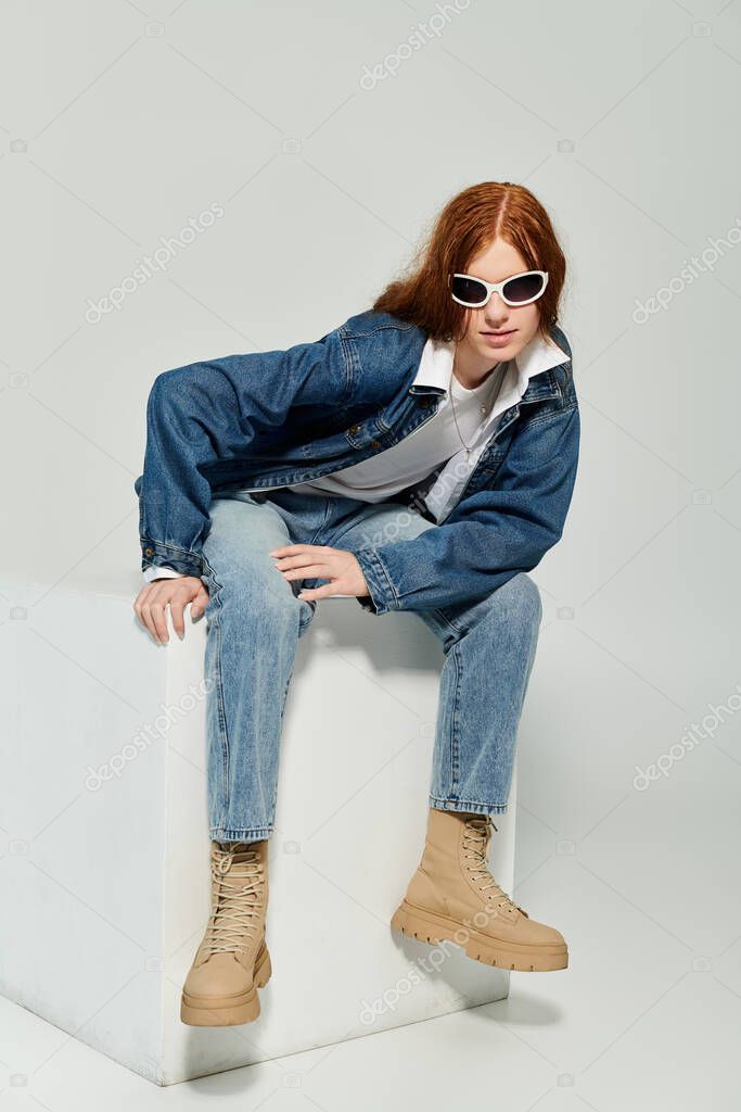 A stylish teenager showcases his chic denim attire while striking a cool pose in a minimalist studio.