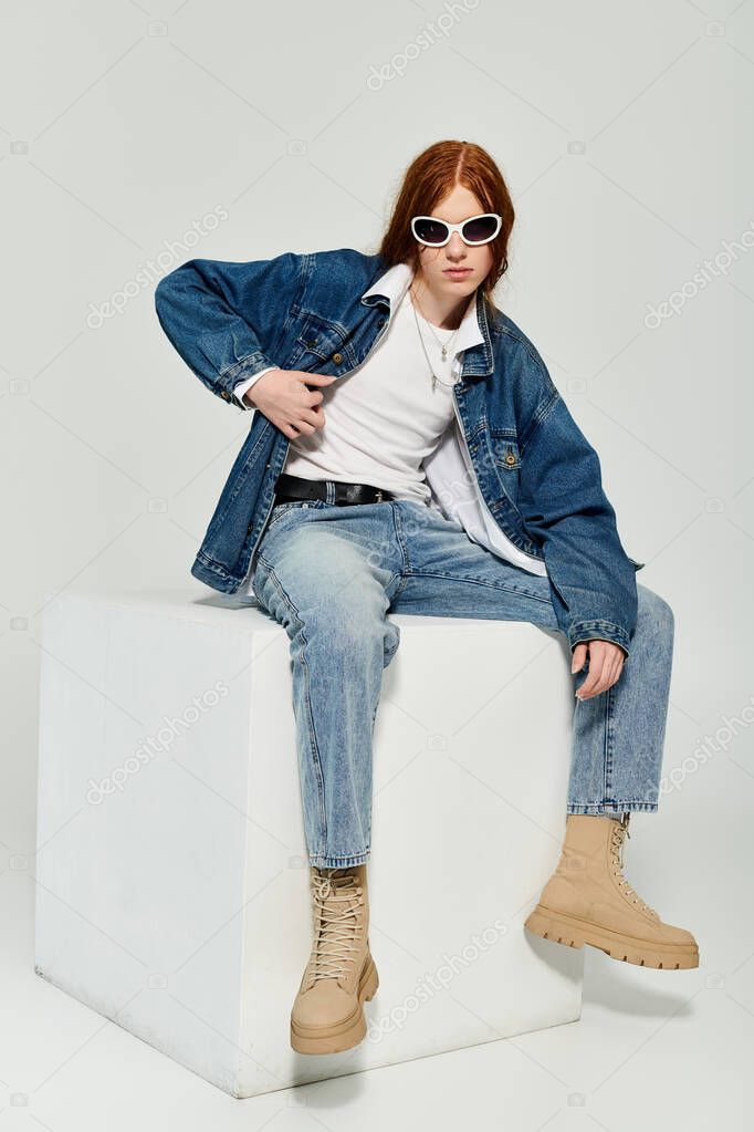 A teenage boy with striking red hair showcases his denim fashion in a vibrant studio setting.