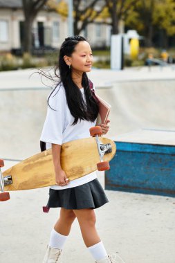 A girl in a chic outfit strolls through an outdoor skatepark, carrying her skateboard and a notebook. clipart