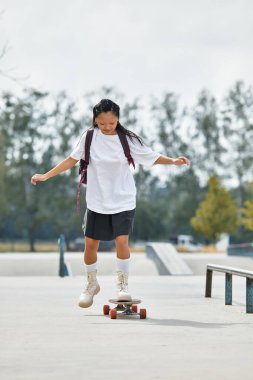 Canlı bir parkta, genç bir kız kaykay yeteneklerini sergiliyor, gençlik kültürünün güneşli gününün tadını çıkarıyor..