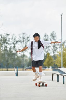 Genç bir Asyalı öğrenci, güneşli bir günün tadını çıkarırken kaykayında ustalıkla dengede duruyor..