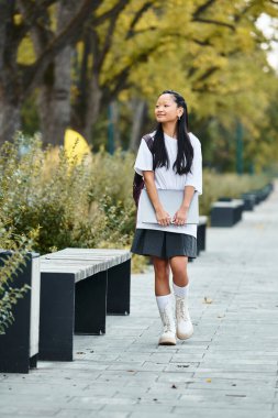 A cheerful girl in a fashionable outfit strolls through a vibrant park filled with autumn colors. clipart