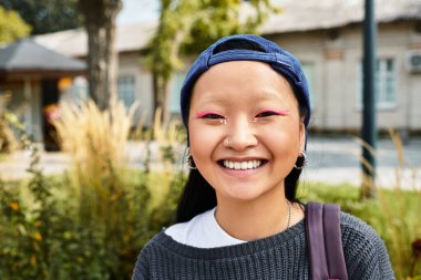 A cheerful young woman showcases her unique style while enjoying a sunny day outdoors in the city. clipart