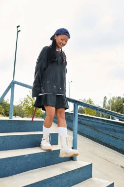 Moda kıyafetli neşeli genç bir kız merdivenlerden aşağı iniyor, şehir merkezinde kendine has tarzını sergiliyor..