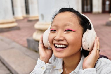 Şık, genç bir Asyalı öğrenci neşeli bir şekilde müzik dinliyor, canlı üniversite atmosferinde sırılsıklam..