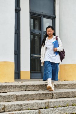 Moda kıyafetleri içinde genç bir kadın üniversite merdivenlerinden iniyor, güven yayıyor ve gençlik kültürünü yakalıyor..