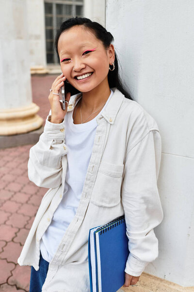 Веселая студентка в модных чатах по телефону, обнимающая университетскую жизнь в яркой атмосфере.