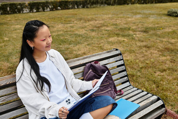 Стильная молодая азиатка улыбается, читая свои заметки в университетском городке.