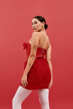 Kırmızı elbiseli kendine güvenen genç bir kadın eşsiz dövmelerini ve çarpıcı güzelliğini sergiliyor..