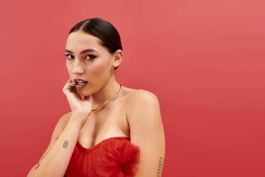 Zarif bir stili olan büyüleyici genç bir kadın zarif kırmızı bir duvara karşı zarafetle poz verir..